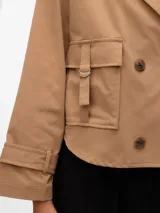 Trench corto color beige con cierre cruzado y bolsillos frontales.