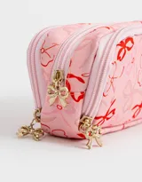 Cartuchera rosa claro con estampado de moños rojos y logo de cerezas. Tiene tres divisiones internas con cierre y tiracierre de moñitos.