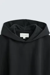Sudadera con capucha negra, de corte oversize, confeccionada en tejido de algodón con interior en rizo. Cuenta con manga larga, bolsillos frontales tipo canguro, efecto lavado y acabados irregulares con vuelta.