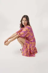 Vestido midi cruzado con estampado floral abstracto en tonos violeta y naranja, con mangas 3/4 abullonadas y lazo ajustable en la cintura. Presenta un tajo lateral.