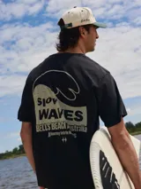 Camiseta negra de algodón con cuello redondo y calce holgado. Estampado en la espalda con una ola y el texto "Slow Waves Bells Beach Australia A Journey into the Waves".