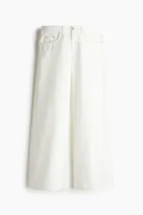Pantalón jean blanco de tiro bajo, corte holgado en cintura y cadera, con cinco bolsillos y pierna ancha.