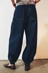 Pantalón bombacho de denim azul oscuro, tiro medio, con trabillas en la cintura, bolsillos delanteros y traseros, pespuntes marcados a contraste, bajo abullonado con puño y cierre frontal con cremallera, botón y ganchos metálicos.