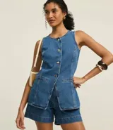 Chaleco de jeans azul, sin mangas, con cuello redondo, cierre frontal con botones dorados, bolsillos delanteros y corte entallado.