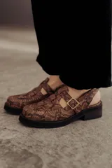 Zuecos de cuero con estampado snake, hebilla lateral metálica, puntera cuadrada y base robusta.