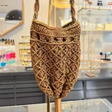 Bolso limosnero marrón tejido en macramé, con flecos largos y asa trenzada.