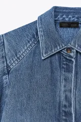 Camisa de denim azul con cuello solapa y mangas amplias tipo kimono. Tiene efecto lavado y cierre frontal con botones ocultos.