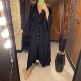 Vestido largo negro con botones frontales, abertura lateral y mangas anchas.