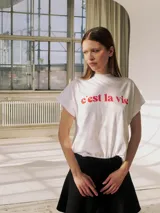 Camiseta blanca de corte holgado con cuello redondo y mangas cortas. Estampado frontal con la frase "c'est la vie" en color naranja.