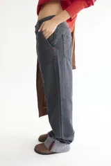 Pantalón de jean gris oscuro, de corte amplio y tiro bajo, con pespuntes rojos a contratono y dobladillo ancho.