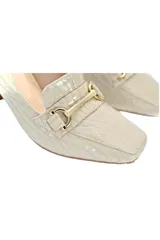 Zapato tipo mocasín color crema con estampado de cocodrilo, punta cuadrada, detalle metálico dorado y taco geométrico de madera.