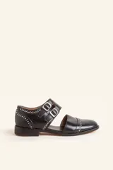 Zapato tipo oxford abierto en los laterales, confeccionado en cuero vacuno negro. Presenta doble tira con hebillas metálicas en el empeine y detalle de tachas plateadas en el contorno del talón y la puntera.