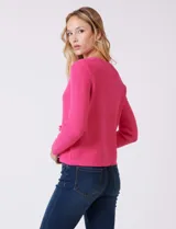 Cardigan tejido color fucsia, con escote a la base y abertura central con botones metálicos dorados. Presenta bolsillos simulados en la parte delantera y terminación desflecada en la abertura y los bolsillos.