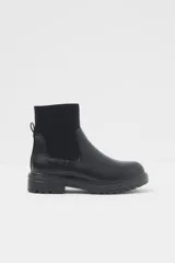 Bota negra de cuero sintético con caña corta, elástico lateral y suela track.