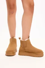 Bota tipo chelsea color camel, confeccionada en gamuza con interior forrado en piel sintética. Presenta elásticos laterales, tirador en la parte trasera y plataforma alta con suela dentada.