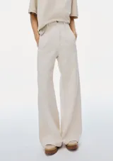 Pantalón de mezclilla color beige claro, de tiro alto y corte ancho (wide leg) que cae recto y amplio hasta el suelo. Presenta cierre frontal y bolsillos laterales.