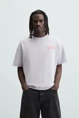 Sudadera lila de corte holgado con cuello redondo y manga corta. Presenta textos estampados en color rojo en el frente y la espalda. Tiene efecto lavado y acabados irregulares.