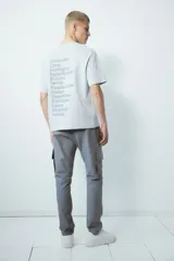 Pantalón cargo gris de sarga de mezcla de algodón, con elástico fruncido en la cintura y cierre con botón a presión. Cuenta con bolsillos al bies con cierre, bolsillo insertado en una pierna, bolsillos con solapa en las piernas y bolsillos insertados atrás. Corte estándar para una silueta clásica y cómoda.