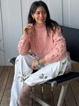 Sweater tejido grueso color rosa, con cuello alto, mangas largas y diseño trenzado con detalles de pompones.