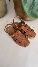 Sandalias bajas color marrón con tiras de cuero entretejidas y hebilla lateral.