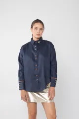 Camisa azul marino de lino con cuello clásico, cierre frontal con botones color madera, mangas largas con puños acampanados y detalle de bordado floral en el cuello.