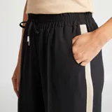 Pantalón negro de tiro alto con corte ancho, cintura elastizada con cordón ajustable y bandas laterales en color crudo.