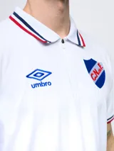 Remera polo azul con cierre, puños y cuello con detalle tricolor. Incluye logo de Umbro y escudo del Club Nacional de Football.