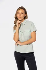 Camisa de lino color verde claro, de corte recto, con cuello camisero, medio abotonado, manga corta y dos bolsillos de parche en el pecho.