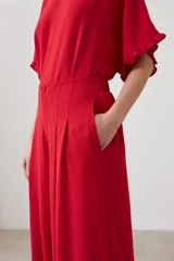 Pantalón palazzo rojo de tiro alto con pliegues marcados en la parte delantera y corte ancho y fluido. La modelo viste un conjunto monocromático con una blusa de manga corta a juego.