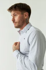 Camisa de hombre a rayas verticales celestes y blancas, corte slim fit, manga larga, logo bordado en el pecho y cartera con botones.