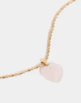 Cadena corta dorada de eslabones torcidos con dije de corazón de cuarzo rosa y cierre de mosquetón.
