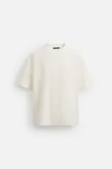 Camiseta color crudo, corte cuadrado, cuello redondo y mangas cortas.