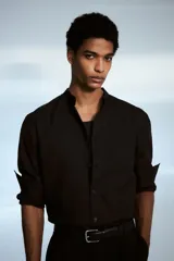 Camisa negra de corte estándar, con cuello mao, tapeta clásica y mangas largas con puños abotonados.