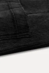 Pantalón ancho de pana color negro, de tiro medio, con trabillas en la cintura, bolsillos delanteros y cierre frontal con cremallera, botón y gancho metálico.
