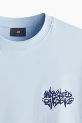 Remera de punto de algodón color celeste claro, con cuello redondo y hombros caídos. Presenta un pequeño estampado en tipografía graffiti azul oscuro en el pecho.