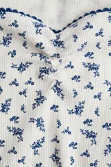 Top corto de punto acanalado fino de algodón color crema con estampado floral azul, mangas cortas y escote corazón con ribete de picot azul.
