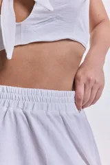 Short blanco con cintura alta y lazo ajustable, con sobrefalda larga asimétrica.