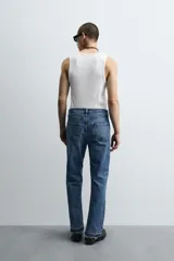Pantalón de jean celeste de corte flare, con tiro medio, cinco bolsillos, cierre frontal con cremallera y botón, y bajo con acabado irregular.