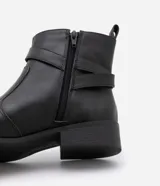 Bota de cuero negro con puntera redonda, caña corta con tirador, cierre lateral con cremallera y detalle de hebilla dorada con doble trabilla.