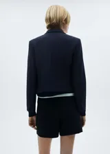 Blazer azul marino con cuello de pico y solapa, diseño crop, bolsillo de parche en el pecho, manga larga con puños abotonados, diseño recto y dos bolsillos de solapa en la parte delantera.