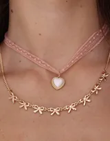 Collar corto doble, uno tipo gargantilla de cinta rosada con dije de corazón y otro dorado con dijes de moños.