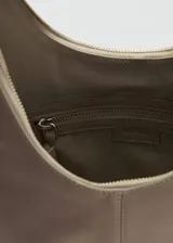 Bolso bandolera grande de cuero color gris topo, con forma de media luna y asa ajustable. Cierre superior con cremallera y forro interior de algodón.
