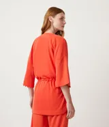 Kimono color naranja de tejido orly con mangas 3/4 con detalle de pompones en el dobladillo, lazo en la cintura y cierre frontal.