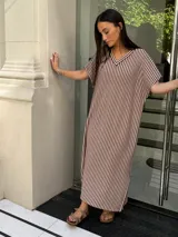 Vestido largo de tejido a rayas horizontales en tonos beige y blanco, con escote en V y mangas cortas tipo murciélago. Presenta tajos laterales en el ruedo.