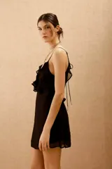 Vestido corto negro con escote en V, espalda descubierta y volados. Confeccionado en viscosa georgette, con breteles finitos que se atan en la espalda y ajuste elástico en la cintura.
