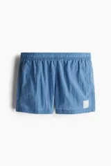 Short de baño azul de nylon con elástico revestido y cordón para ajustar oculto en la cintura, bolsillos laterales y bolsillo de solapa con cierre autoadherente atrás. Largo por encima de la rodilla con abertura corta en los laterales y suspensor interior en malla suave.