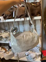 Bolso tipo hobo de cuero color oro macchiato, con correa de hombro ajustable y cierre superior con cremallera.