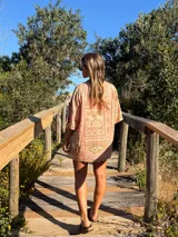 Camisa oversize de manga corta con cuello camisero y botones frontales. Confeccionada en tejido estampado con motivos marinos y texto en tonos rosados y beige.