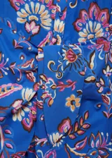 Vestido camisero azul con estampado floral en tonos rosa, naranja y marrón. Tiene cuello mao, cierre frontal con botones, mangas largas con puños abotonados y lazo decorativo en la cintura.
