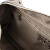 Cartera tipo baúl color gris, confeccionada en cuero sintético texturizado. Cuenta con doble asa de mano, correa bandolera regulable y extraíble, cierre superior, herrajes plateados, un bolsillo interno con cierre, dos bolsillos internos abiertos y forro de tela de algodón y poliéster.